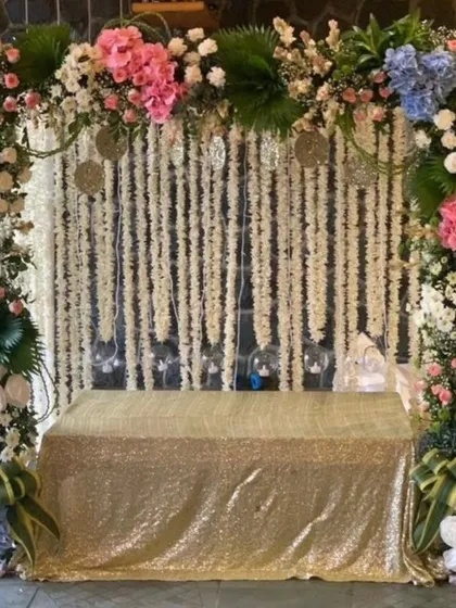 This setup combines sparkle and flowers for a truly festive look. The gold sequin cloth and colorful floral frame make it perfect for Navratri or Diwali.