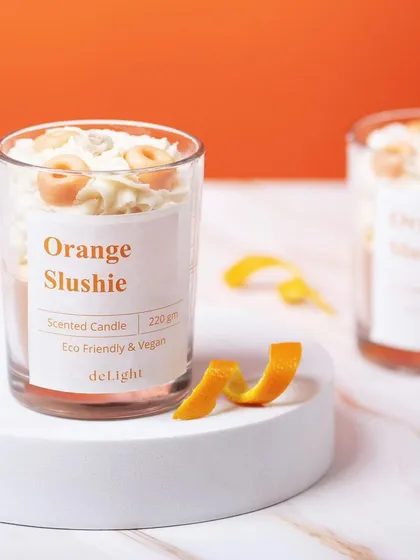 A vibrant shot of an Orange Slushie scented candle. The bright orange background and orange peel props create a zesty, refreshing, and fun image.