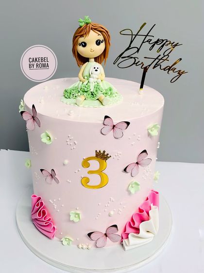 A pretty pastel pink cake for a 3rd birthday. The design includes a custom girl figurine with her pet dog, surrounded by delicate butterflies and flowers.