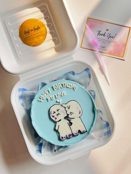 A cute and intimate bento cake design showing two stick figures sharing a kiss, with the message "Happy Birthday My Love" on a soft blue background.