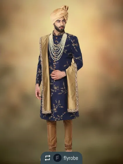 A stunning navy blue sherwani with gold floral embroidery, paired with a gold stole and a multi-layered pearl mala. This is a perfect look for an evening wedding ceremony.