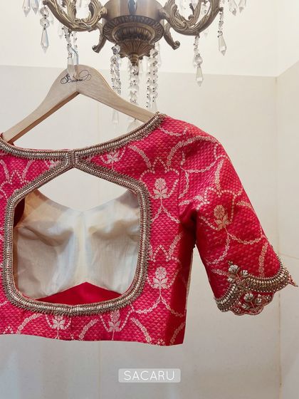 The back of the crimson red and off-white blouse, featuring a large square cutout framed with intricate zardosi work.