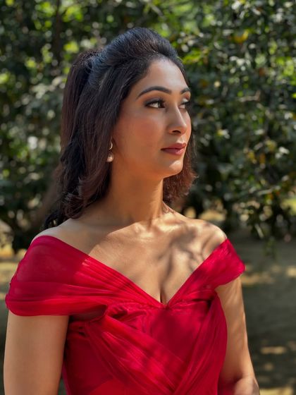 A client looking radiant in a red off-shoulder dress. The makeup is fresh and sun-kissed, perfect for an outdoor day event.