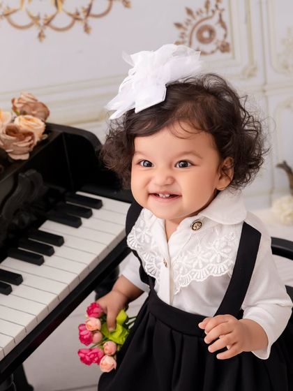Flower in hand, music in soul. This little girl's bright, toothy smile is the star of this classic piano-themed portrait.