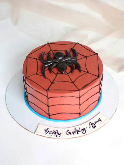 A simple and clean Spider-Man themed cake. The design features a red cake with black spiderweb piping and a bold black spider, perfect for a young superhero fan.