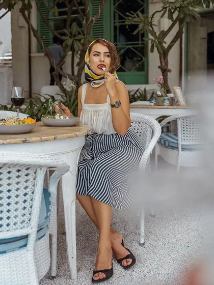 A candid-style shot of a woman dining at Olive Bistro. The vintage-inspired styling with a headscarf and the action of eating create a narrative of enjoying 'la dolce vita'.