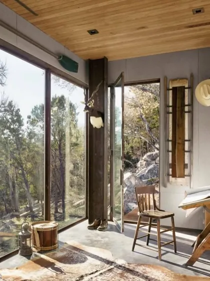 The interior of this rustic cabin offers a peaceful retreat with stunning forest views. The large windows and natural materials create a warm and inviting atmosphere, perfect for a quiet escape.