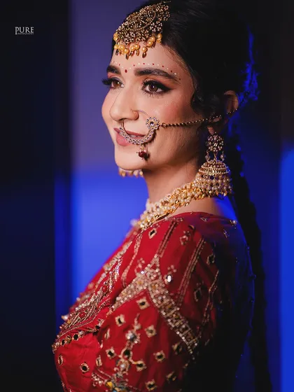 A profile shot of the bride against a cool blue background. This modern lighting technique makes her traditional red and gold attire pop.