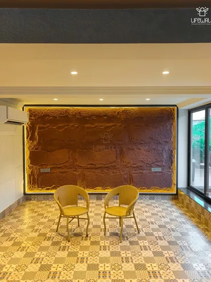 The interior of a glass house featuring a unique textured stone wall with backlighting, creating a dramatic and earthy focal point.