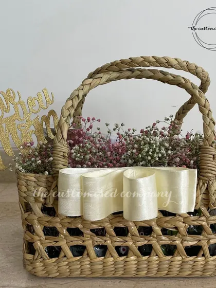 A beautiful and simple arrangement featuring baby's breath in a woven jute basket, accented with a concept bow and a "Love You Mom" cake topper. We can create custom floral concepts for any occasion.