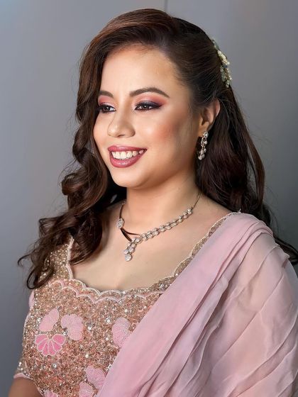 A soft and pretty party look in shades of pink. The makeup features a pink and purple smokey eye and a rosy lip, paired with soft curls and a delicate hair accessory.