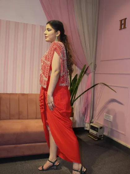 A side profile of the red draped skirt set, showing how the jacket flows.