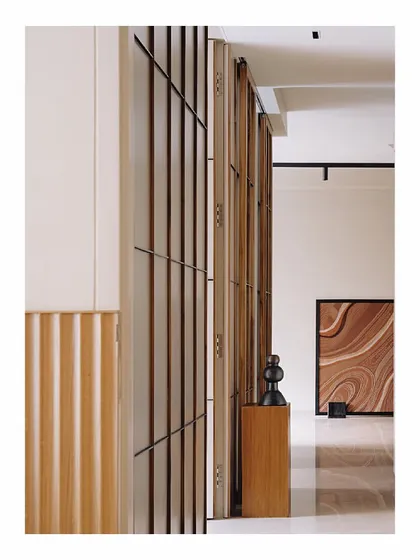 This wall is clad in paneling inspired by Japanese shoji screens, using thin teak wood verticals and black metal batons. It discreetly hides several doors and storage spaces, creating an illusion of a single, continuous surface that adds length to the passageway.