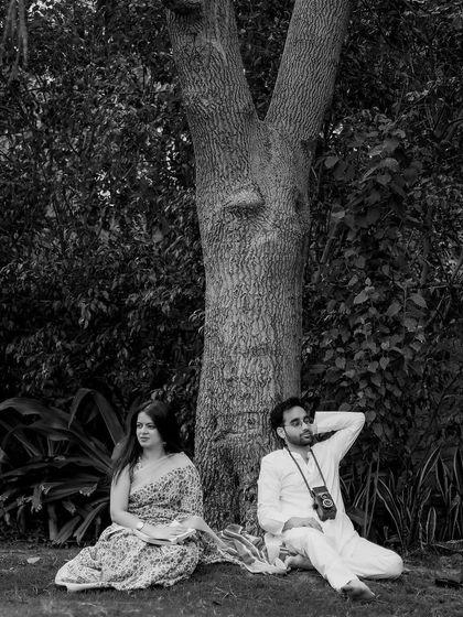 A peaceful moment of rest under a tree. This black and white photograph has a quiet, contemplative mood, capturing the couple in a moment of shared tranquility.