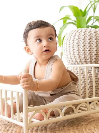 A baby boy sits in a miniature bed prop during a boho-themed indoor session.