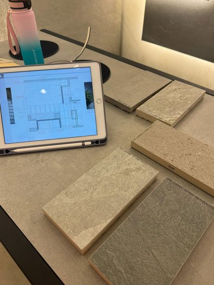 Reviewing stone tile samples for a project, comparing their color and texture against the digital floor plan on an iPad. This ensures the chosen materials work within the larger design scheme.