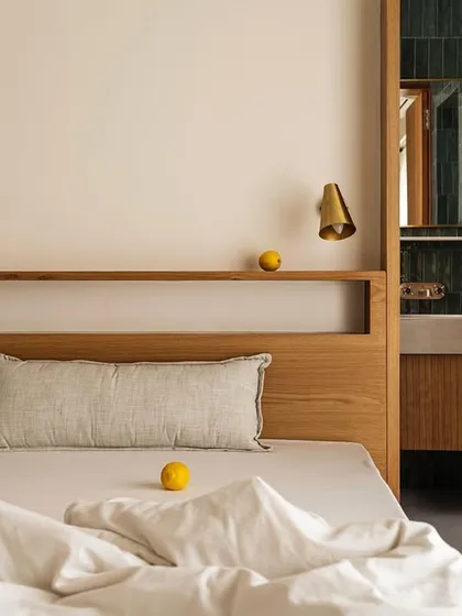This bedroom in Apartment 1005 features a custom oak headboard with an integrated shelf. A pass-through window offers a view into the ensuite bathroom, which is clad in rich green tiles, creating a visual connection between the two spaces.