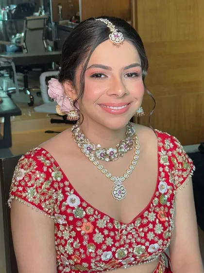 Malvika's happy smile says it all. Her natural bridal makeup is paired with a simple updo and a delicate pink flower, creating a look of effortless beauty.