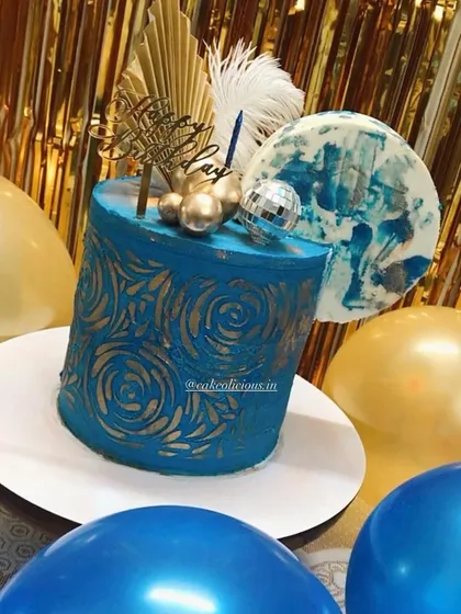 An asymmetrical cake I made for my brother's birthday. This modern design features a bold blue ganache with a gold stenciled pattern, topped with a disco ball, feathers, and an abstract chocolate sail.