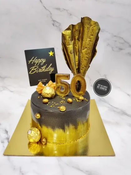 Celebrating 50 years in bold black and gold. This cake features a modern brushed metallic effect, a dramatic chocolate sail, and Ferrero Rocher chocolates for a touch of classic indulgence.