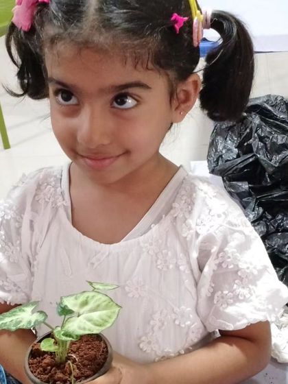A young girl holds up the small plant she potted during a summer camp activity, learning about gardening and responsibility.