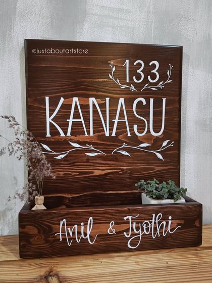 A different angle of the "Kanasu" name plaque, showing the fine details of the lettering and the small plants that bring it to life.