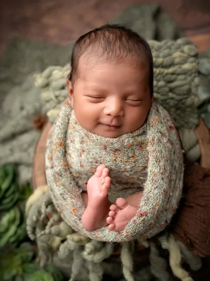 A smiling newborn with the cutest little feet peeking out. This shot, with its earthy green tones, is full of warmth and joy.