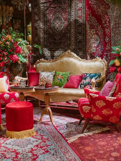 Another seating arrangement combines a vintage carved sofa with bold red armchairs and ottomans. The backdrop of layered Persian rugs adds to the rich, eclectic, and luxurious atmosphere.