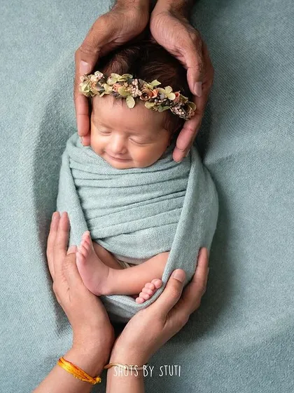 A newborn held safely in parents' hands, with a gentle, smiling expression. This pose is a beautiful way to show the love and protection surrounding your baby.