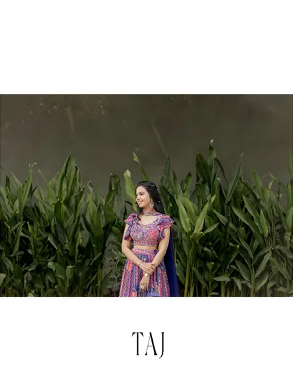 A beautiful solo portrait of the bride against a lush green backdrop. The simple, elegant framing highlights her colorful lehenga.