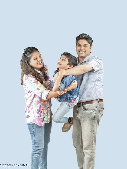 A playful and candid moment as parents lift their laughing son, showcasing a fun and energetic family dynamic against a simple light blue studio background.