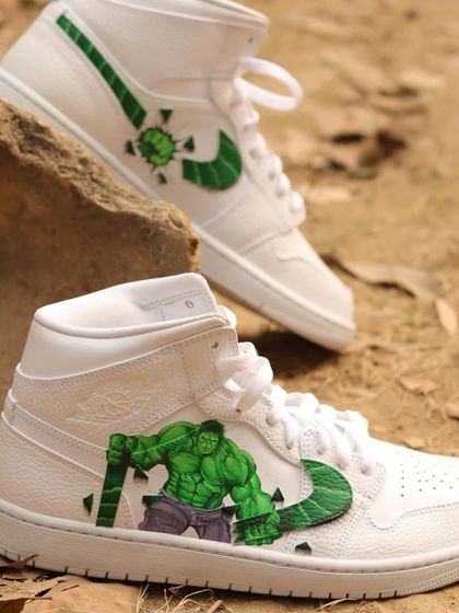 A full shot of the custom Hulk Air Jordan 1s. One shoe features the Hulk smashing the swoosh, while the other shows his fist breaking through, creating a dynamic and cohesive pair.