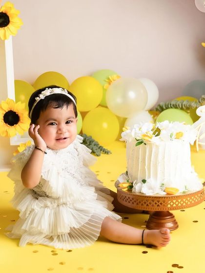 This little darling is ready for her cake smash. The bright yellow background and sunflowers create such a happy and vibrant atmosphere for a first birthday photoshoot.