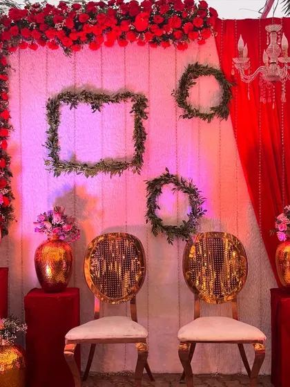 A quirky and fun photo booth with a red and white theme. The design includes framed greenery, chandeliers, and elegant gold chairs, offering a stylish spot for pictures.