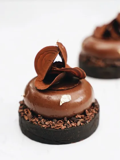 A sophisticated chocolate tart with delicate chocolate shavings. This minimalist shot on a white background highlights the elegant pastry work and rich texture.