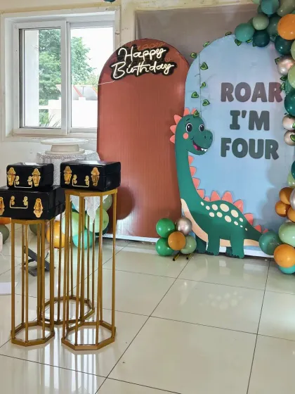 "Roar I'm Four!" A cute dinosaur-themed birthday setup. This decor uses arched backdrops and a balloon garland in shades of green and orange to create a playful prehistoric scene.