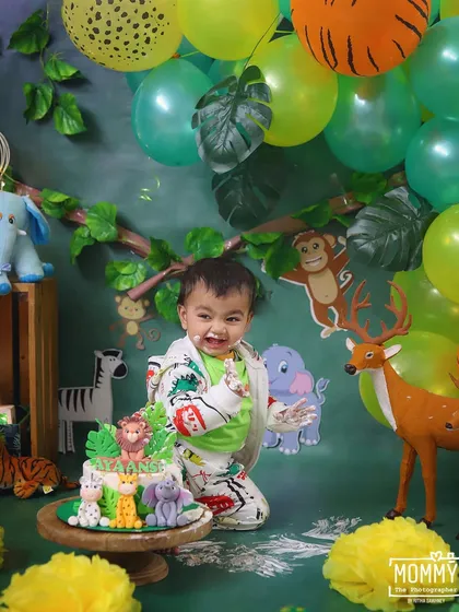 Welcome to the jungle! This little one is having a wild time during his jungle-themed cake smash. The big smile and messy cake face are what these fun first birthday photoshoots are all about.
