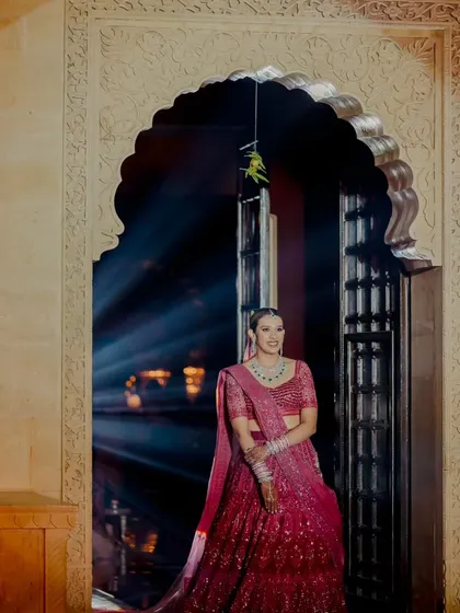 A bride makes a dramatic entrance through an arched doorway, illuminated by a single spotlight. This theatrical moment, set against the stone architecture of Suryagarh, is the definition of a grand bridal entry.