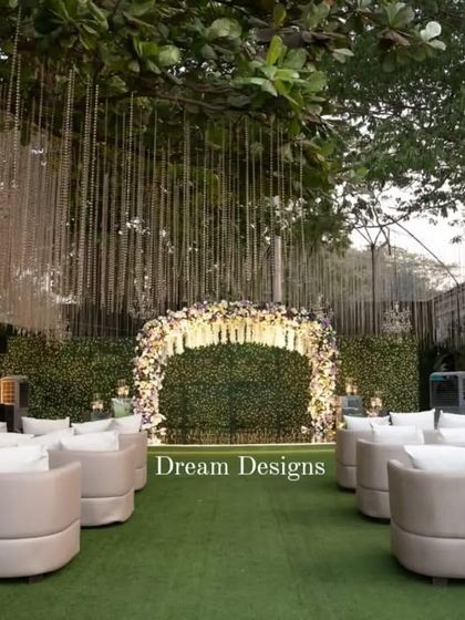 This reception seating arrangement features modern, curved white sofas facing a floral arch backdrop. The combination of comfortable lounge seating and beautiful decor creates an inviting and stylish space for guests to mingle.