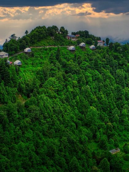 A wide shot of the Kanatal dome stay, capturing the property under dramatic sun rays breaking through the clouds. This image highlights the magical, dream-like quality of a glamping adventure.
