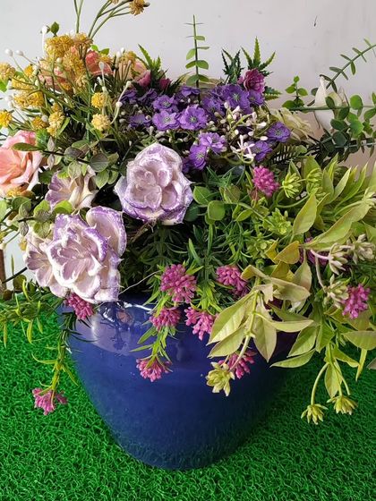 This bouquet showcases a mix of purple, pink, and yellow artificial flowers, creating a rich and textured look. Set in a blue ceramic pot, it’s a maintenance-free way to enjoy a garden-fresh feel indoors.