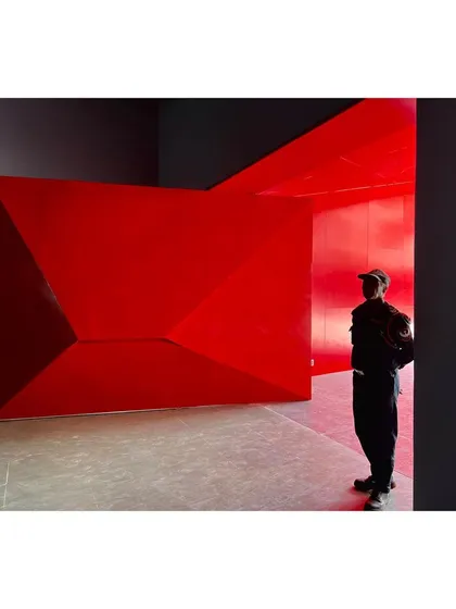 A security guard stands beside the monumental red entrance door of the university sports center. The folded metal form creates a dramatic and memorable entry sequence.