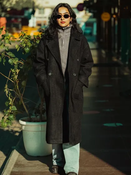 A full-body street style shot of a model in a long black overcoat and sunglasses. This demonstrates our ability to shoot high-impact, edgy looks on location.