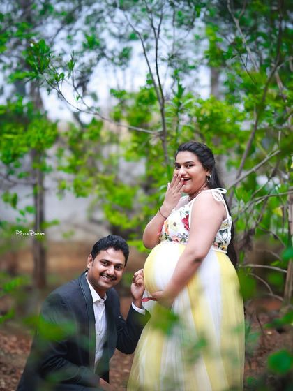 A fun and candid outdoor shot of a couple, with the dad-to-be playfully pointing at the baby bump.