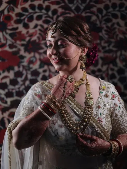 Adjusting the final details. Every piece of jewelry, from the nath to the layered necklaces, is carefully placed to create a balanced and regal bridal portrait.