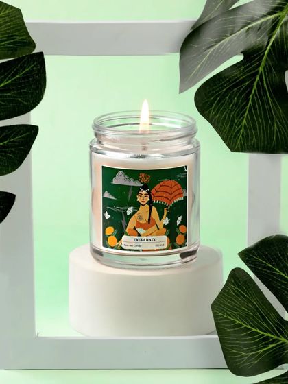 Framed by monstera leaves, this "Fresh Rain" candle evokes a lush, tropical vibe. The clean, green and white color palette gives the image a refreshing and natural feel.