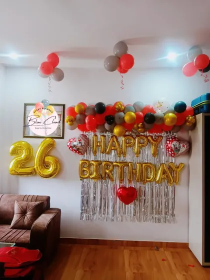 A 'Happy Birthday' wall decoration with a shimmer curtain and a garland of red, grey, and gold balloons.