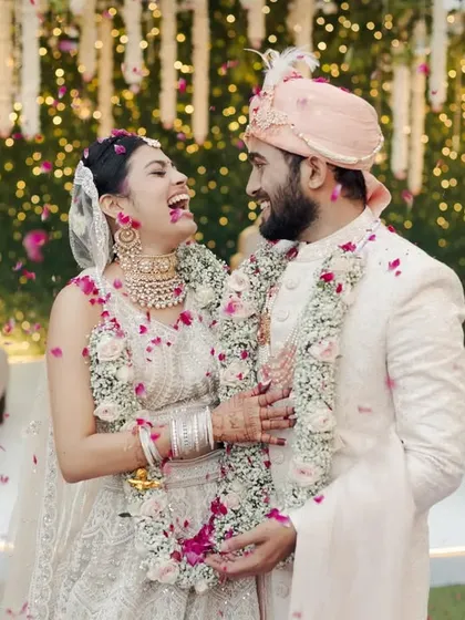 A joyous moment captured right after the varmala ceremony. The couple is showered in petals against a backdrop of hanging white flowers and a lush green wall.