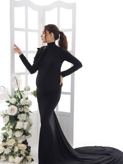 A full-length view of the elegant black gown. The simple, clean lines of the dress and the bright background create a modern and sophisticated maternity portrait.