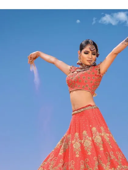 A dramatic shot of the coral-red zardosi lehenga, capturing the bride's powerful and celebratory spirit against a brilliant blue sky.